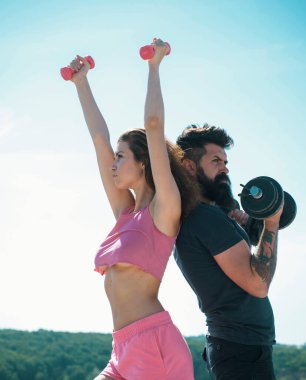 Sporty woman in sexy pink sportswear. Sportive fitness couple, bearded man and sexy woman working out outdoors, sportive couple training with dumbbells, muscular coupl outdoor