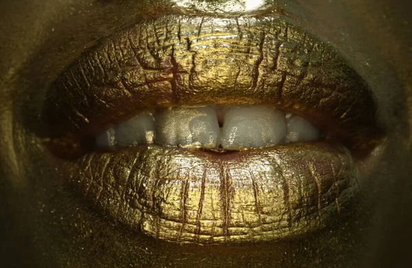Golden lips macro close up. Gold lips. Gold paint from the mouth. Golden lips on woman mouth with make-up. Sensual and creative design for golden metallic