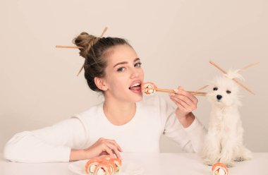 Japon suşi tarzı. El ele tutuşan genç kadın Makizushi suşi rulosu, geleneksel Japon yemekleri izole edilmiş stüdyo portresi. Kadın ve yavru köpek ellerinde çubuklarla suşi yiyorlar.