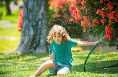 Mutlu çocuk hortumdan su döküyor. Bahçede çiçekleri sulayan çocuk. Evde bahçe işleri.