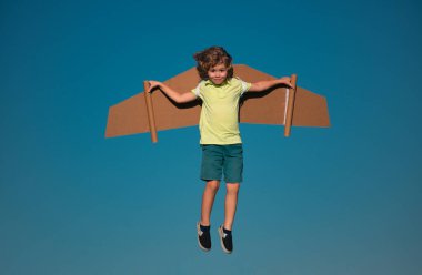 Yazın gökyüzü arka planında oyuncak kanatlarla oynayan çocuk