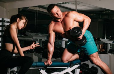 Antrenman bisepsleri. Spor salonunda ağır halterlerle çalışan kişisel antrenör kadın. Spor adamı konsepti. Çıplak gövdeli sportif bir erkek. Egzersizler. Güçlü atletik vücut