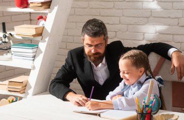 Sınıfta öğretmen olan ilkokul öğrencisi. Öğrenci kız, öğretmeniyle birlikte ders çalışıyor ve yazı yazıyor. Okul malzemeleriyle masasının yanında gülen surat ifadesiyle sevimli kız dersleri alıyor.