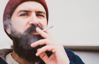 Şehir dışında sigara içen yakışıklı bir adamın yakın portresi. Sigara içen sakallı adam.