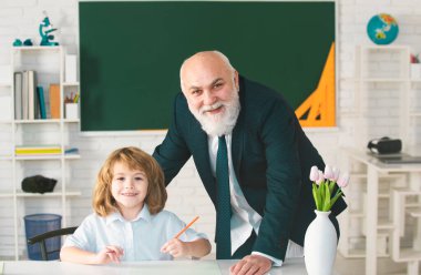 Yaşlı öğretmen ve genç öğrenci veya okul çocuğu. Öğrenci sınıfta öğretmenle okuma yazma öğreniyor.