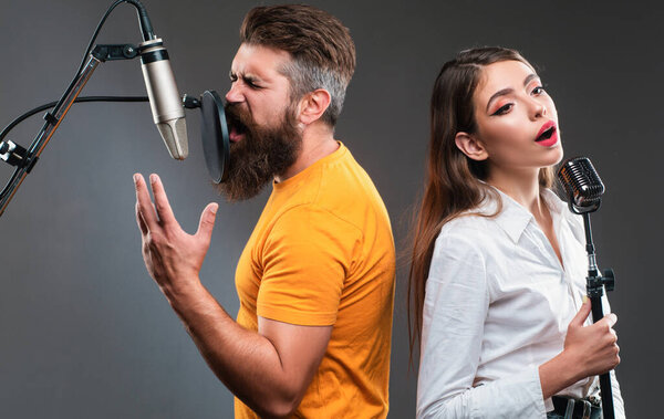 Singer duet couple is performing a song with a microphone while recording in a music studio