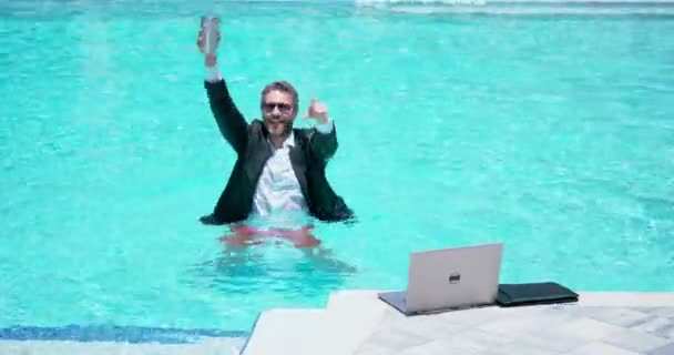 在游泳池里穿着手提电脑的商人 一个疯狂的商人在暑假 在游泳池里穿着湿衣的兴奋的商人 有趣的商人 滑稽的生意 远程在线工作 — 图库视频影像