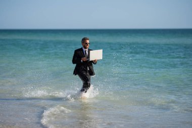 Leisure weekend and remote freelance work. Crazy comic business man in suit rest on sea bech. Funny businessman with laptop runnig on water. Remote summer business. Summer holiday for businessman