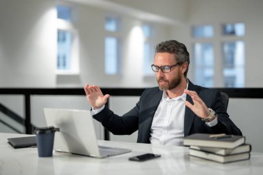 Ofisinde dizüstü bilgisayarı olan bir iş adamı. Modern ofiste çalışan uzaktan kumandalı personel. İş adamı çevrimiçi toplantıda. İnternette çalışan İspanyol iş adamı. İş yerinde laptop kullanan olgun bir iş adamı