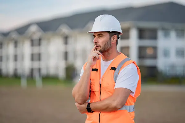 Builder thinking. Portrait of builder in a construction site. Builder ready to build new house. Construction builder wear building uniform and helmet