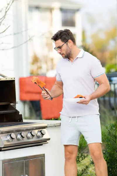 Cook man preparing barbecue grill outdoor. Man cooking tasty food on barbecue grill at backyard. Chef preparing food on barbecue. Millennial man grilling meat on grill. Bbq salmon fillet