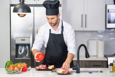 Modern mutfakta yemek pişiren adam. Adam evde ev işi yapıyor, mutfakta kahvaltı hazırlıyor. Yakışıklı adam mutfakta yemek pişiriyor. İspanyol adam mutfakta sağlıklı yemek pişiriyor.