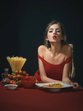 Makarna yiyorum. Makarna yiyen genç bir kadının portresi. Kadınlar soslu spagetti yerler. Makarna güzel. Kız spagetti yiyor. Sağlıklı beslenme. Seksi bir mutfak. Ağzında spagetti ye.