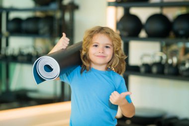 Spor salonunda yoga minderi tutan zinde bir çocuk. Yoga çocuk konsepti. Güçlü atletik fitness çocuğu. Çocuk Spor Konsepti