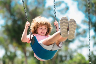 Küçük çocuk yaz günü parkta salıncakta sallanırken eğleniyor. Mutlu çocuk sallanmaktan zevk alır. Anaokulunda oyun parkında oynayan çocuk. Çocuk parkında neşeli bir çocuk