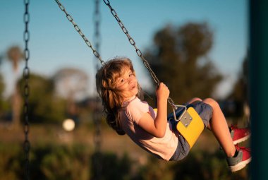 Children swinging on the playground. Cute little kid boy funny while playing on the playground. Summer, childhood, leisure and children concept