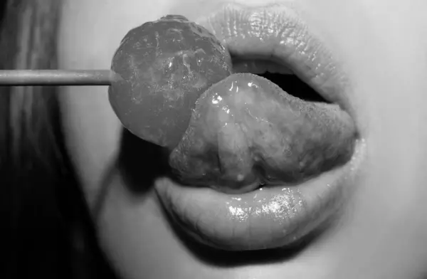 Lollipop in the mouth, close-up. Beautiful girl mouth with lolli pop. Glossy red woman lips with tongue. Mouth lick suck chupa chups