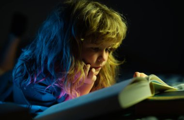 Yatakta uzanmış kitap okuyan sevimli bir çocuk. Çocuğun gelişimi. Akıllı çocuk.