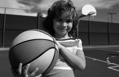 Sevimli gülümseyen çocuk basketbol oynuyor. Aktif çocuklar basket topuyla dışarıda oyun oynuyorlar. Sportif çocuk portresi