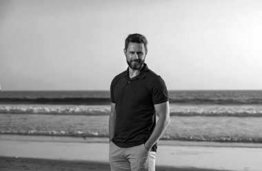 Sahildeki bir adamın portresi. Ciddi bir ifadeyle orta yaşlı bir adamın portresi ve sahilde duran okyanus manzarası.