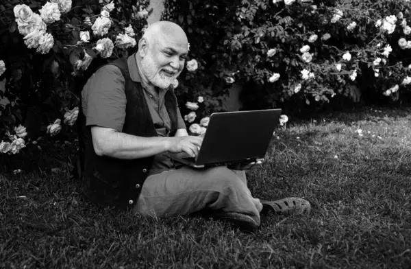 Telework concept. Senior man in garden with laptop. Old gardener online social network games