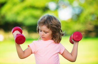 Çocuk parkta egzersiz yapıyor. Aktif çocuk, sağlıklı bir yaşam tarzı var. Güçlü pazı kasları olan spor çocuğu halter egzersizi yapıyor.