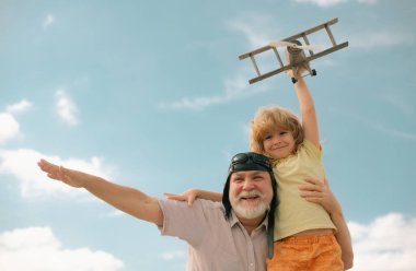 Grandfather and grandson having fun with plane outdoor on sky background with copy space. Child dreams of flying, happy childhood with granddad