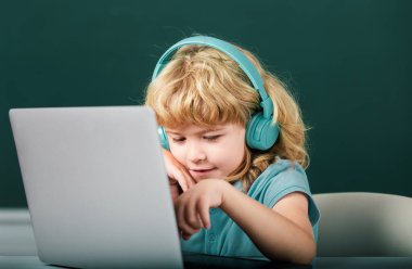 Kulaklıklı akıllı çocuk masada oturur, okulda dizüstü bilgisayarda çalışır, klever çocuk internet derslerini kullanarak öğrenirken kulaklık takar. İlkokul ve eğitim