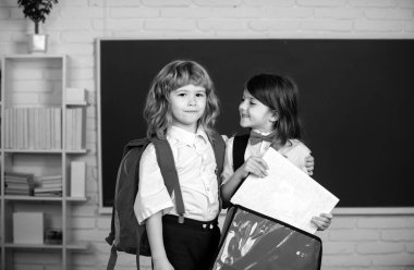 School friends learning together. Schoolgirl and schoolboy in classroom at school. Kids friends with backpack in school class near blackboard. Concept of friendship and classmate. Best school friends