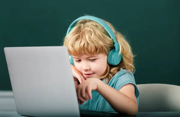 ヘッドフォンのスマートボーイは机に座って 学校でラップトップでオンラインで勉強し 賢い子供はインターネットのレッスンを使用してノートブック学習でイヤホンを着用します 小学校 — ストック写真