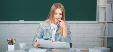 Lisede ya da üniversitede ders veren kız öğrenci. Kopya alanı olan karatahta arkaplan üzerine kitap okuyan kız öğrenci