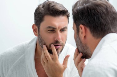 Tıraş olduktan sonra mükemmel cilt teması olan seksi, şehvetli bir erkek. Cilt bakımı kozmetik işlemleri konsepti. Aynaya bakan adam, hassas cilt, kozmetik tedavisi. Cilt bakımı