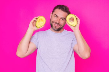 Mutlu Adam taze avokadonun yarısını pembe arka planda, stüdyo resminde izole etti. Avokado. Sağlıklı görünüş. Yakışıklı bir adamın portresi Avokado 'yu yüzüne yakın tutar.