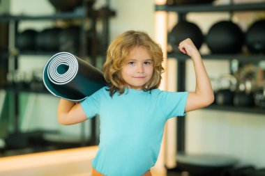 Kolları güçlü olan heyecanlı çocuk spor salonunda yoga minderi tutuyor. Yoga çocuk konsepti. Genç, güçlü, sportif çocuk. Spor sporu konsepti.