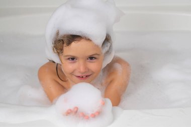 Banyo köpüğüyle yıkanan çocuk. Tatlı çocuk banyo yapar, beyaz bir banyoda sabun köpüğü ve şampuanla yatar.