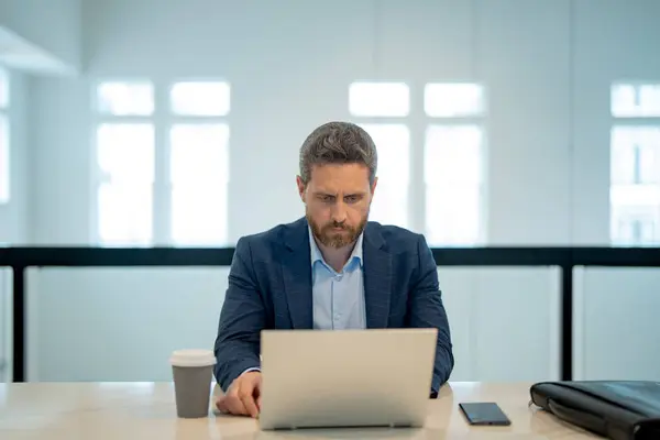 オフィスにノートパソコンを持ってる男 オフィスでスーツを着たビジネスマンがノートパソコンで働いている ノートパソコンを使ったオフィスワーカー ビジネスマンはノートパソコンで働いている ビジネスマンは現代のオフィスのインテリアでオンライン作業を持っています — ストック写真