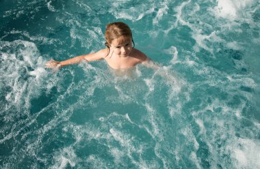 Havuzda gülümseyen küçük sevimli çocuk. Çocuk plaj tatilinde suda oynuyor.