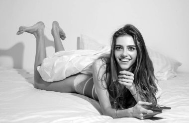 Gülümseyen genç kadın yatakta mesaj atıyor. Mutlu bayan evde uzanmış, cep telefonu kullanıyor ve gülümsüyor, kopyalama alanı kullanıyor. Akıllı telefondan sosyal medyada sohbet etmek veya kontrol etmek