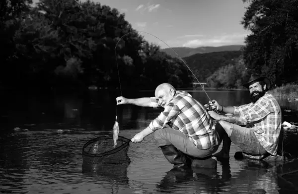 Catching fish. Father and mature son fisherman fishing with a fishing rod on river