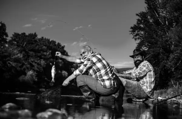 Catching fish. Young and old fisherman standing on the shore of lake with fishing rod. Father and son enjoy life. Men family, granddad and drandson fishing. Mature man fisher celebrate retirement