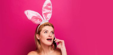 Tavşanlı Paskalya bayrağı. Paskalya tavşanı. Pembe arka planda izole edilmiş cep telefonlu genç bir kadın.