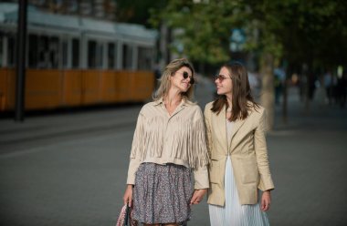 İki heyecanlı mutlu kadın sokakta birlikte yürüyor. Şehirde mutlu moda kızları var. Olumlu ifade eden neşeli genç kadınlar, neşeli duygularla tatil, harika bir ruh hali.