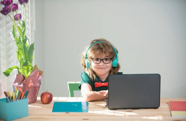 Child boy in headphones using a laptop at home. Homeschooling, online distant learning