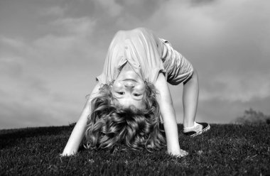 Yeşil çimlerin üzerinde baş aşağı duran mutlu çocuk. Gülen çocuk bahar parkında eğleniyor. Sağlıklı çocuk yaşam tarzı konsepti