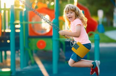 Child playing on outdoor playground. Kids play on kindergarten yard. Kid boy having fun on outdoor playground. Colorful playground with a swing, slide, climbing ladder