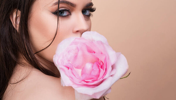 Fashion portrait of young beautiful woman with blue eyes and pink rose. Close-up portrait of a beautiful young girl with a pink rose near face