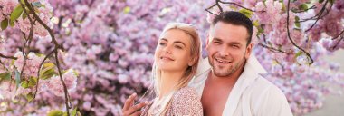 Aşık bahar çifti, Banner. Aşıklar romantik anlar yaşıyor. Şehvetli kadın ve erkek yaz çiçekleri parkında pembe çiçekler içinde