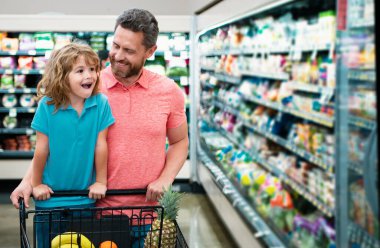 Baba ve oğul markette ürünlere bakıyor. Baba ve çocuk süpermarketten yiyecek alıyor.
