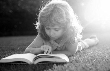 Portrait of happy child boy with book in park. Kids early education. Little kid read book in the garden. Summer vacation homework. Preschool student education. Smart clever Kids