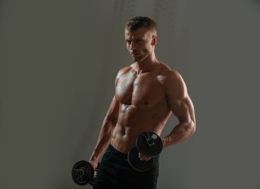 Sportif gövde, dambılı adam. Karanlık stüdyoda dambılla egzersiz yapan genç bir sporcunun portresi. Crossfit, spor ve sağlıklı yaşam tarzı konsepti